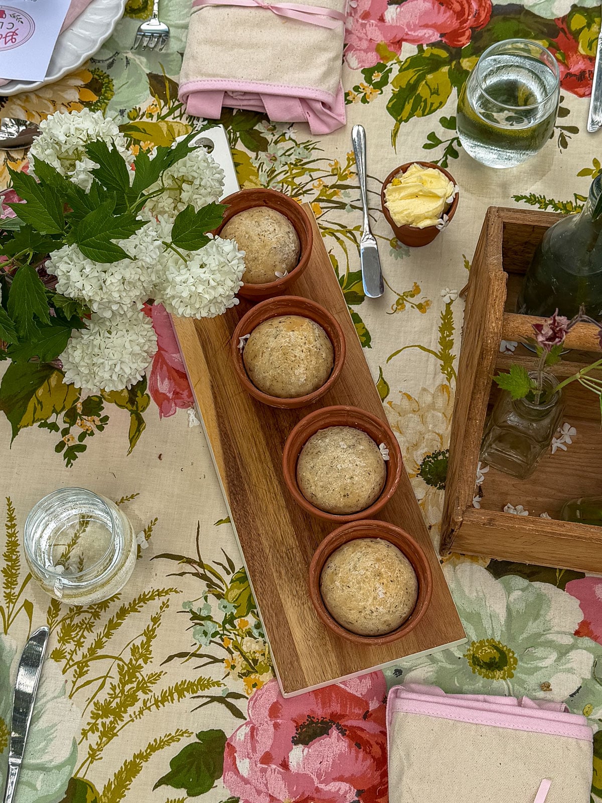 Four individual herb breads baked in terracotta flower pots on wooden tray beside small flower pot butter dish and white hydrangea blossoms.