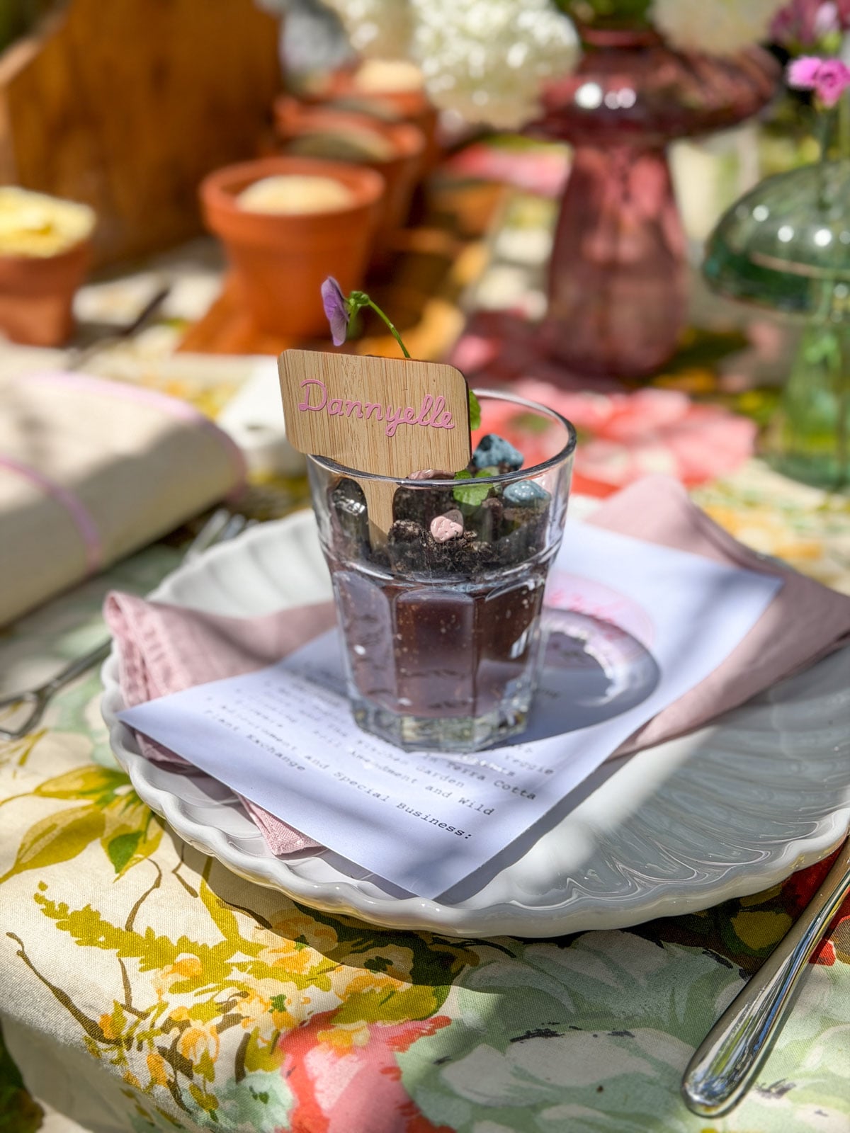 Dirt pudding placecard cup with personalized bamboo plant label on white scalloped plate with pink linen napkin and Garden Club agenda card.