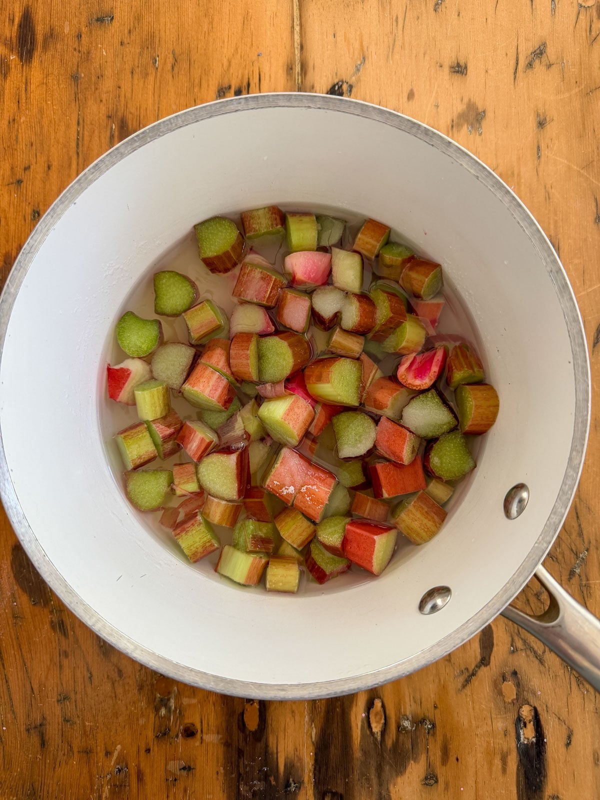Chopped fresh rhubarb pieces with sugar and water in a white saucepan ready to simmer into rhubarb simple syrup.