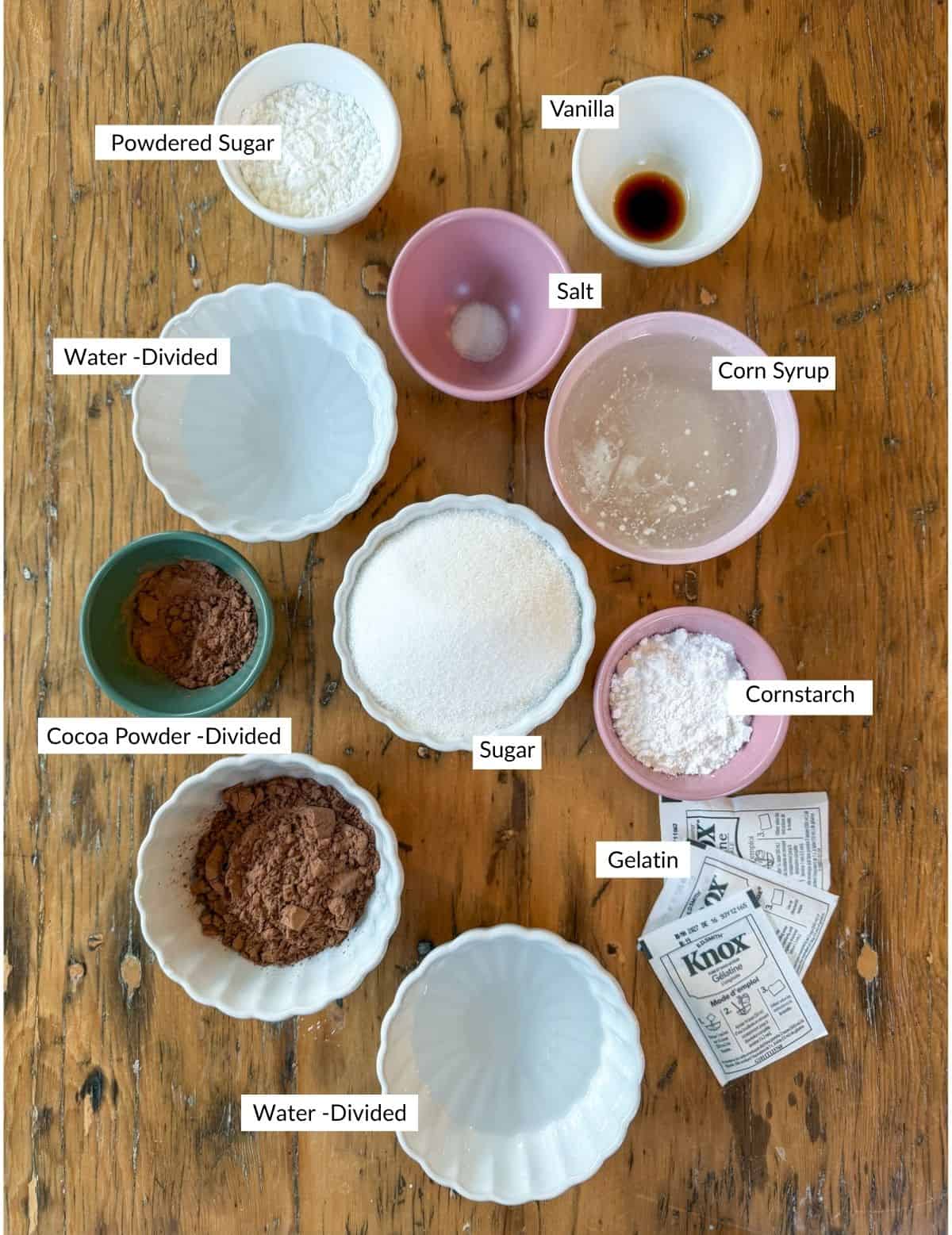 Ingredients for chocolate marshmallows in bowls on a wood table.