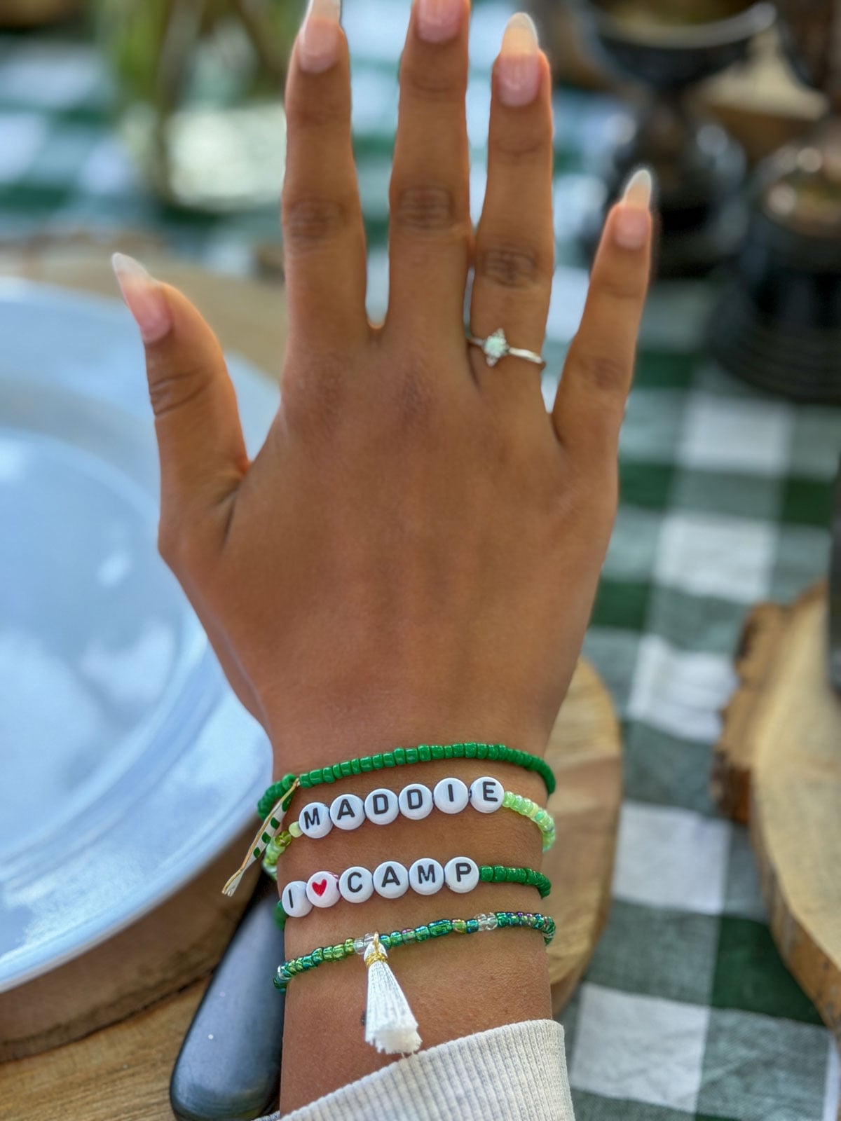 Hand wearing green beaded friendship bracelets spelling Maddie and I Heart Camp.