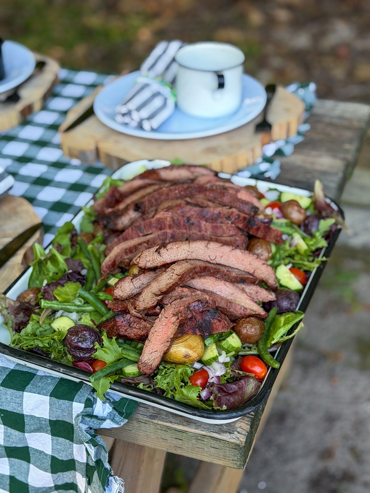Sliced grilled flank steak over mixed greens, potatoes, and cherry tomatoes.