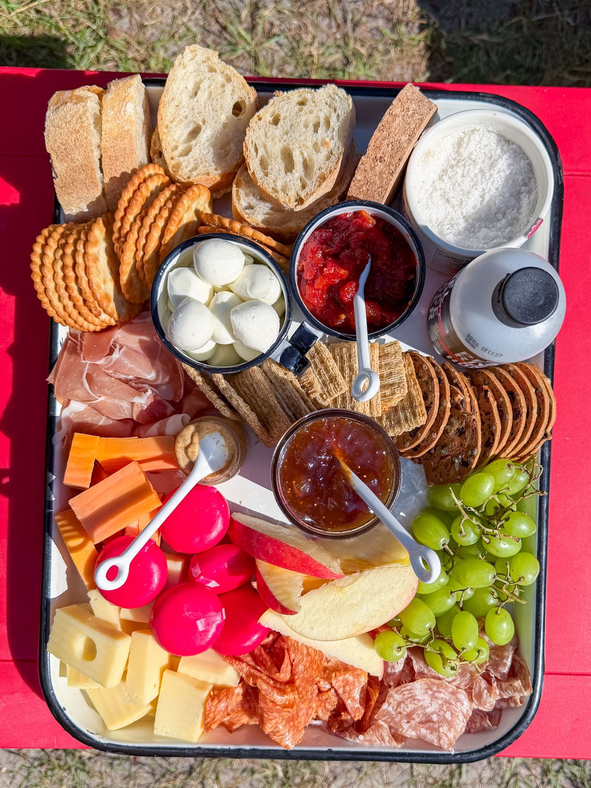Savory s'mores spread with crackers, mozzarella, prosciutto, jam, and cheese on a red table.