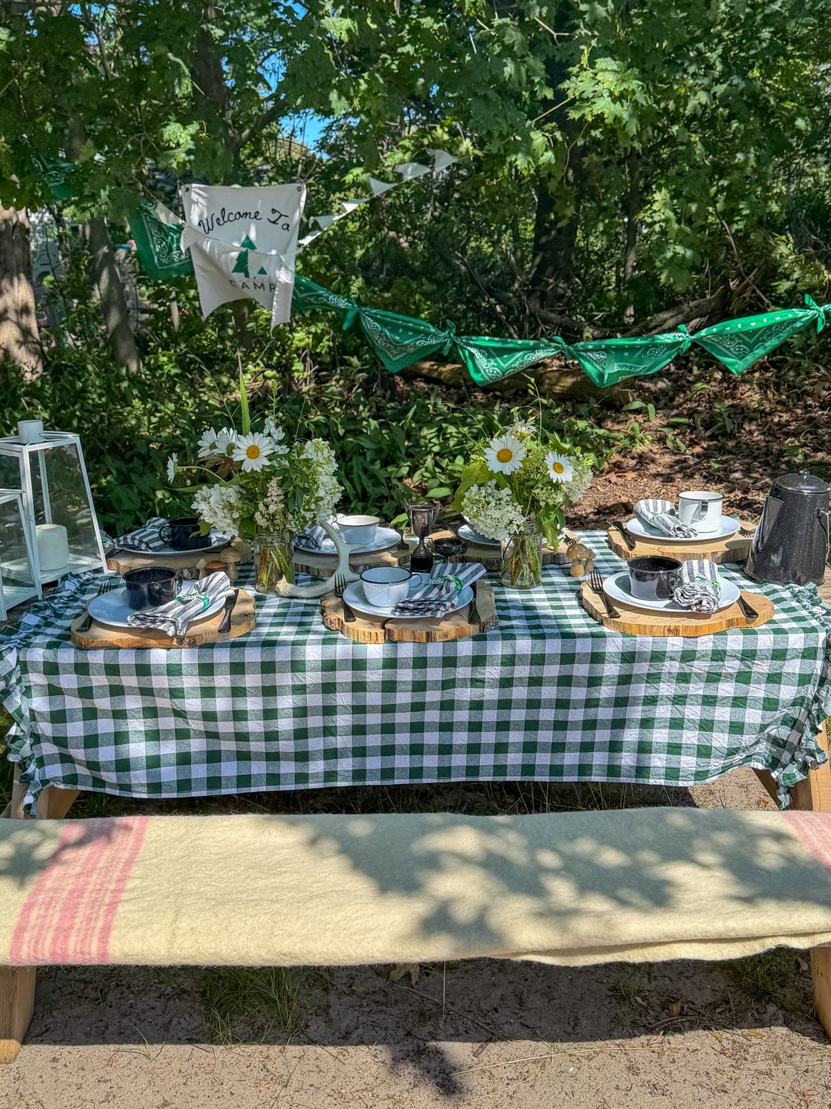 Camp themed party table with green gingham tablecloth, wildflowers, enamelware, and Welcome to Camp banner.