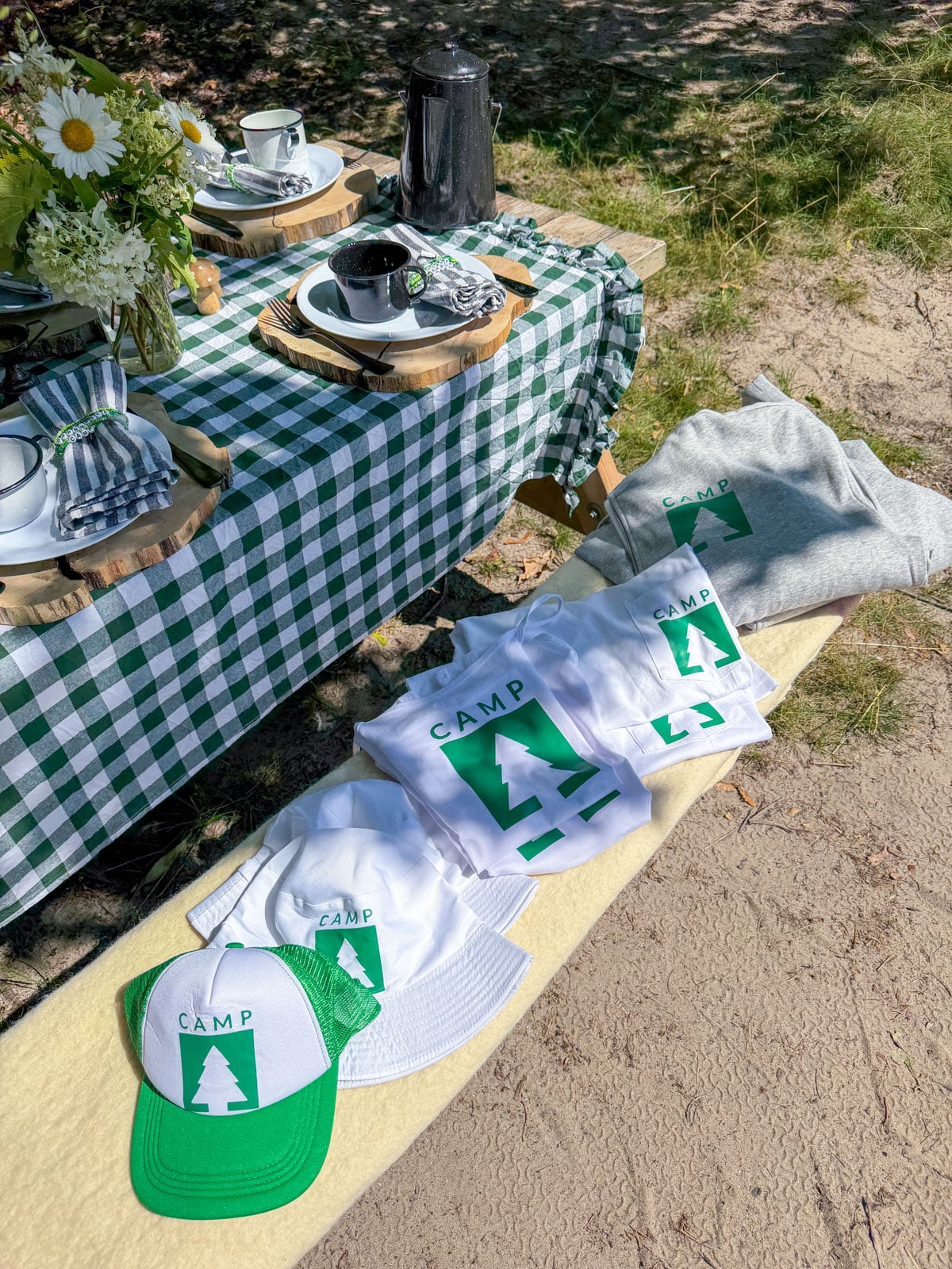 Folded green and white Camp logo hoodies, t-shirts, and trucker hats.