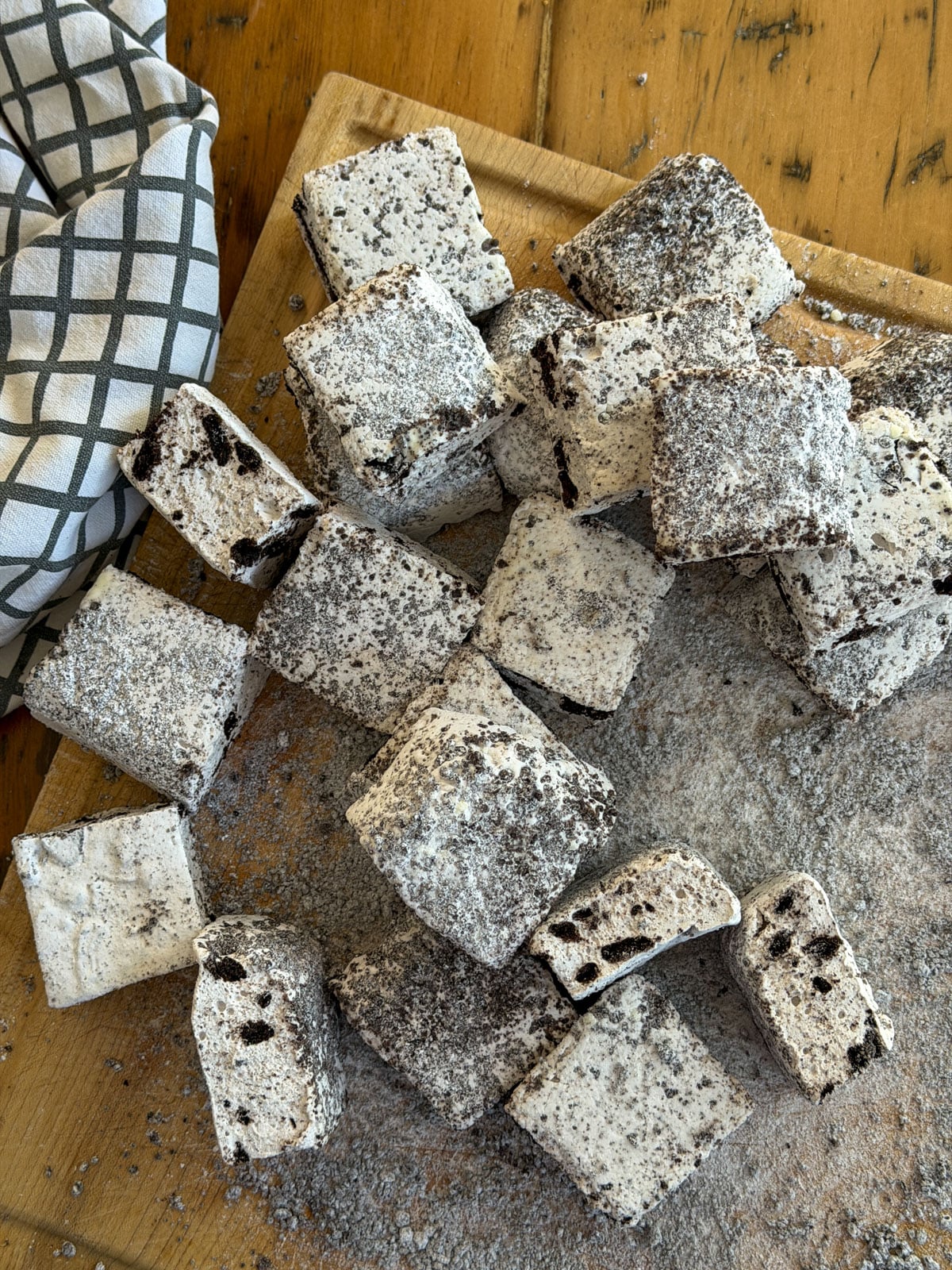 Cut Oreo marshmallow squares piled on a wood board with a kitchen towel.