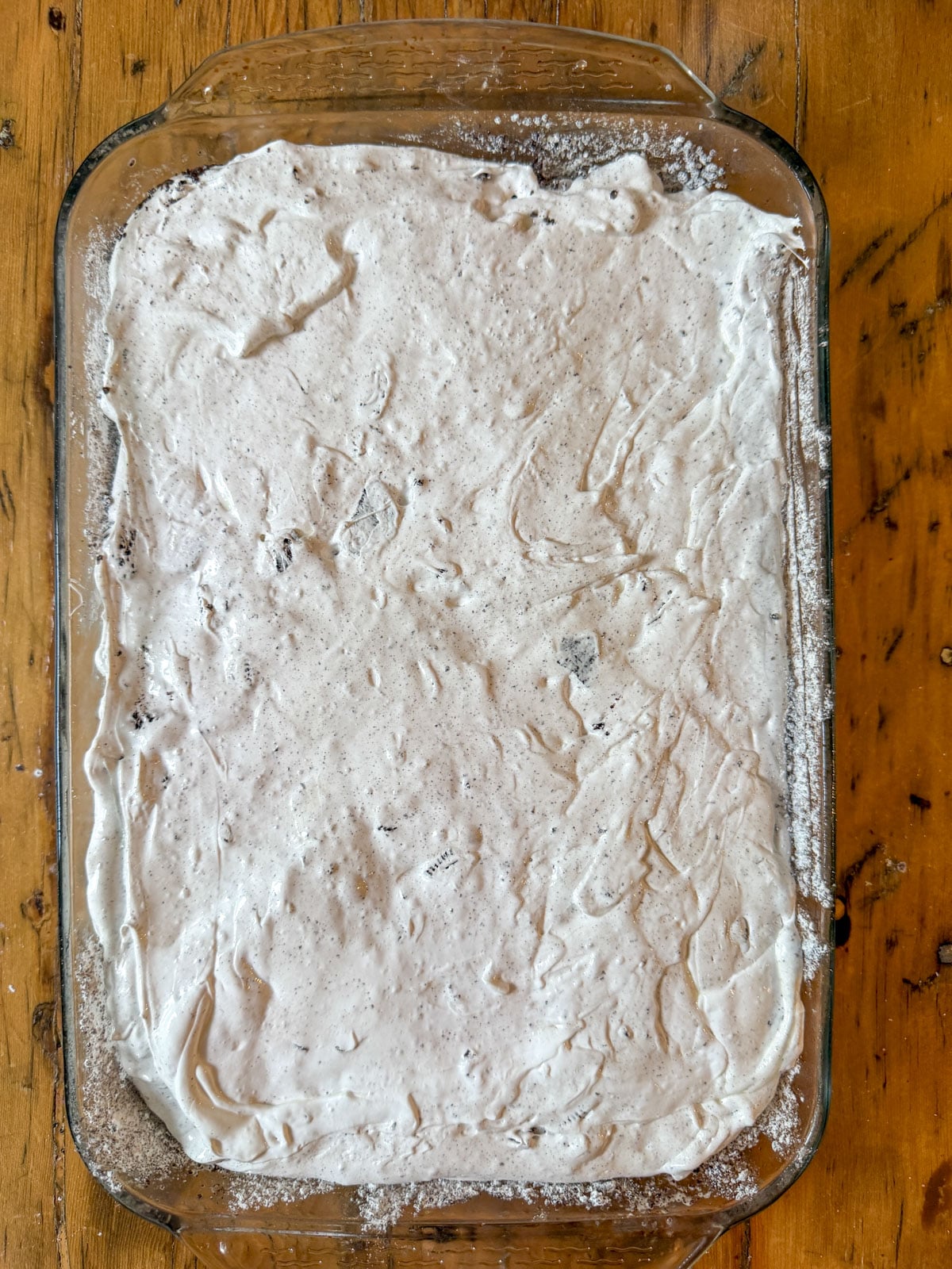 Oreo marshmallow mixture spread smooth in a glass baking pan.