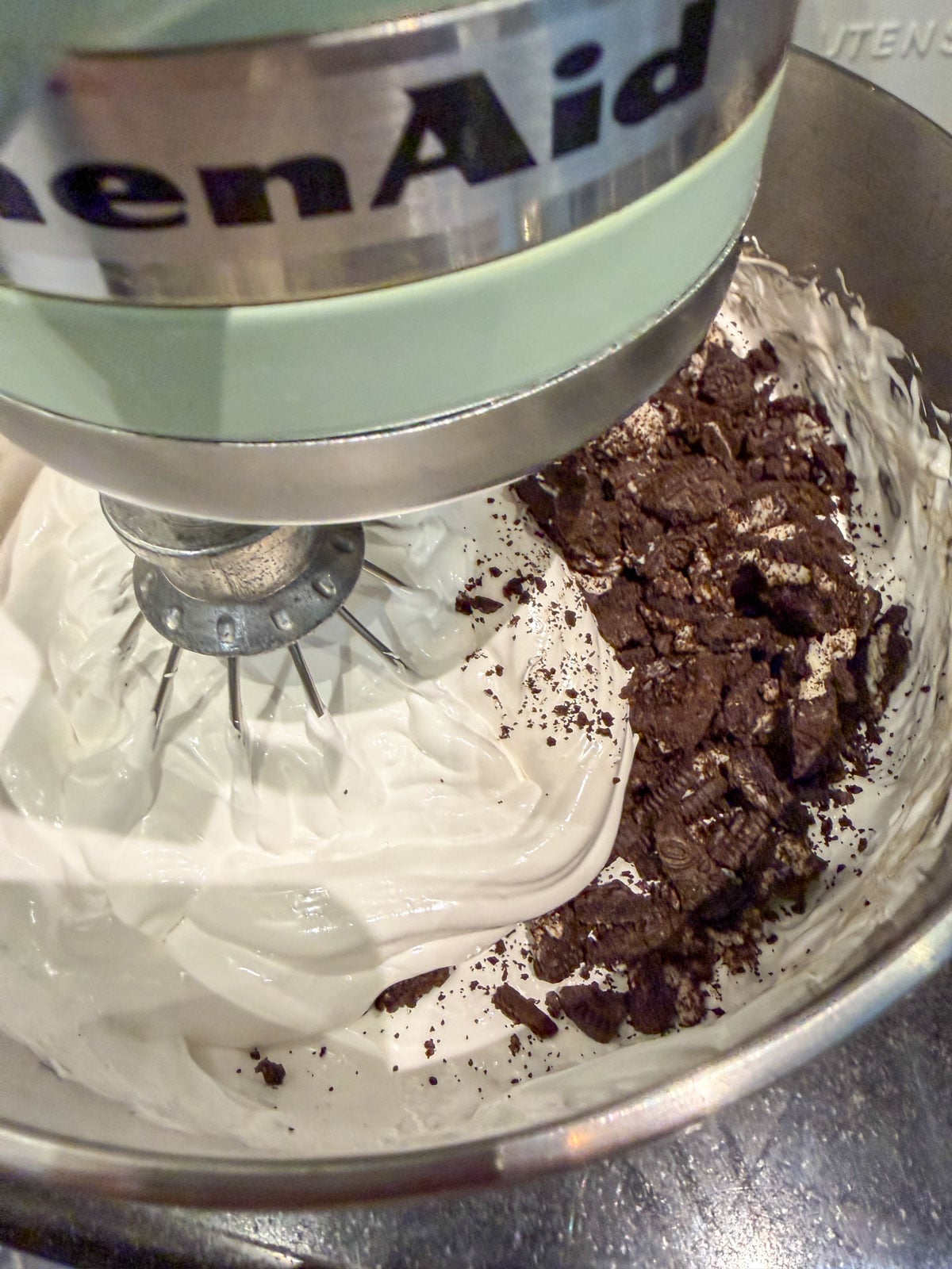 Chopped Oreo cookie pieces being folded into whipped marshmallow.
