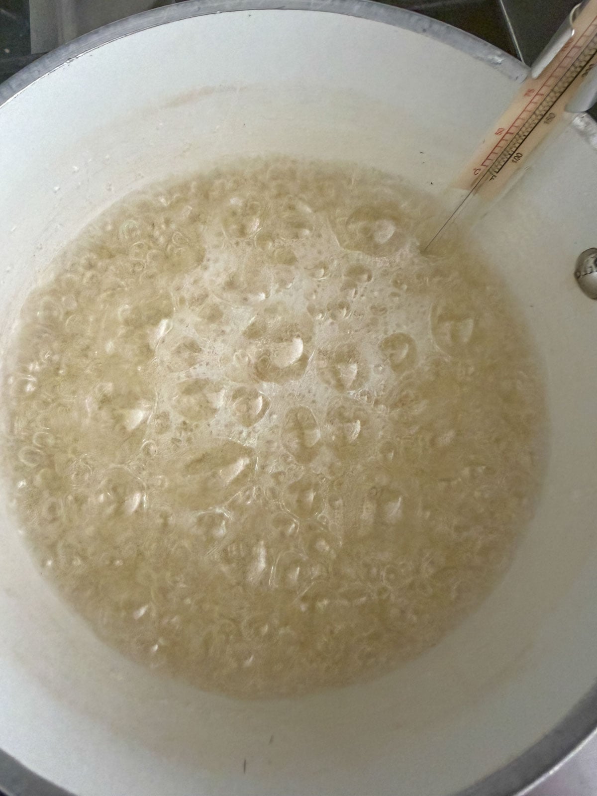 Sugar syrup boiling in a saucepan with a candy thermometer.