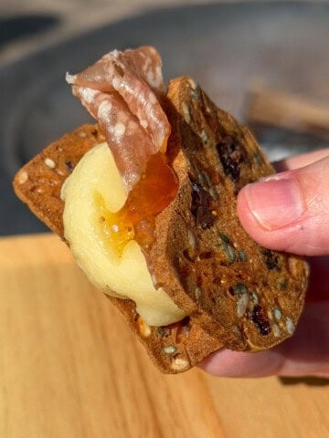 Melted cheddar and apple savory s'more held in hand with hot honey drizzle.