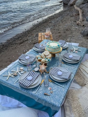 Adult mermaid party table set on the beach with cake and shells.