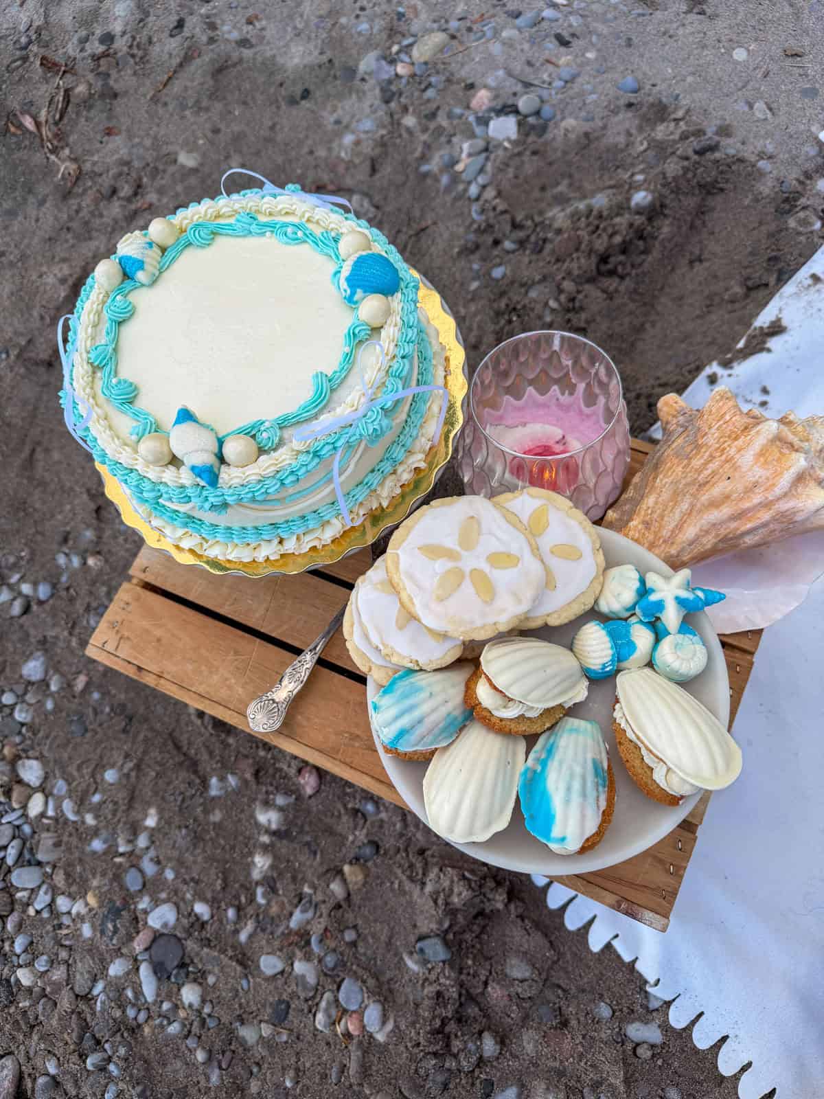 Mermaid cake and seashell cookies on a wooden crate at the beach.