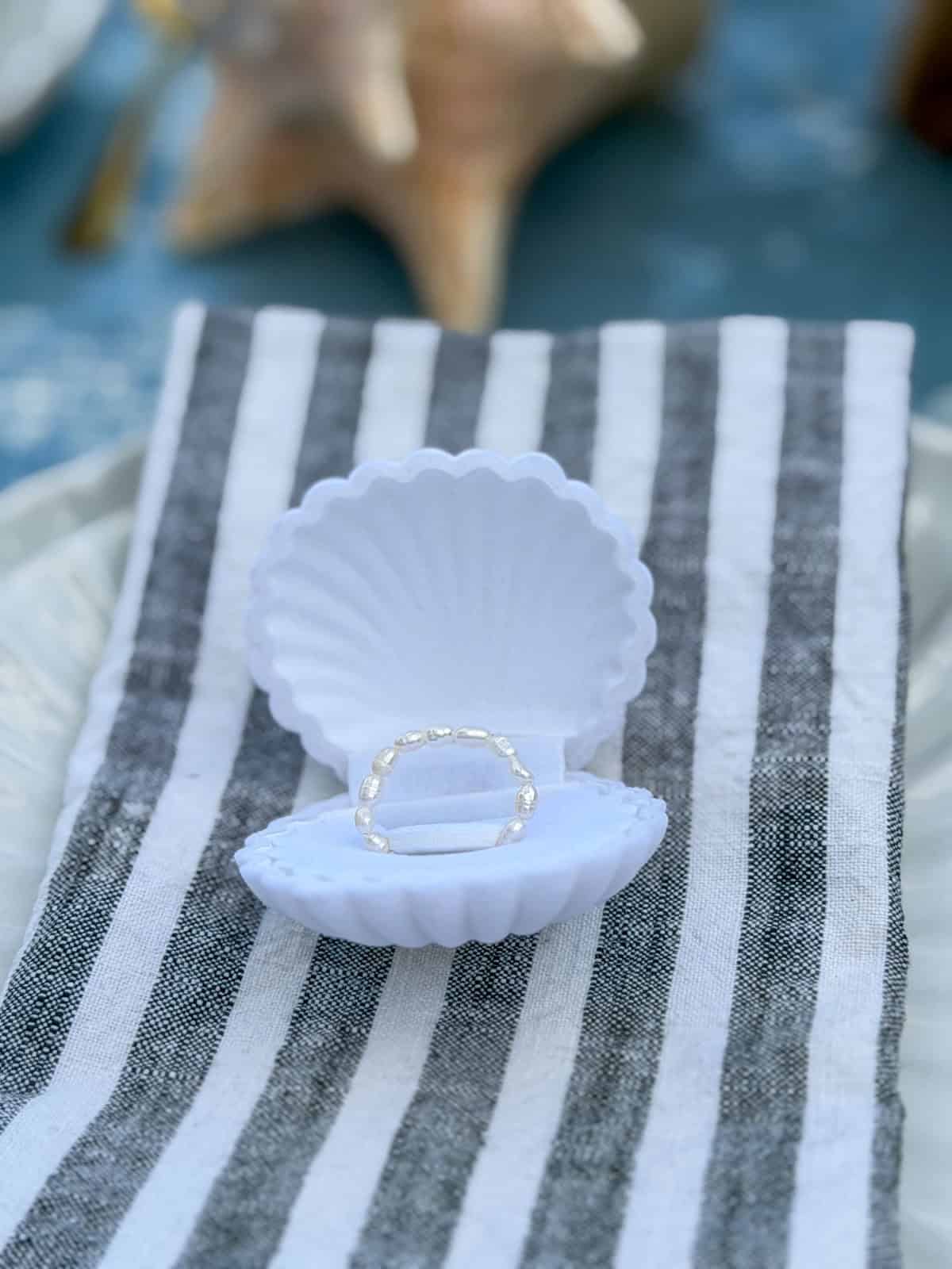 Freshwater pearl ring in a white shell ring box on a napkin.