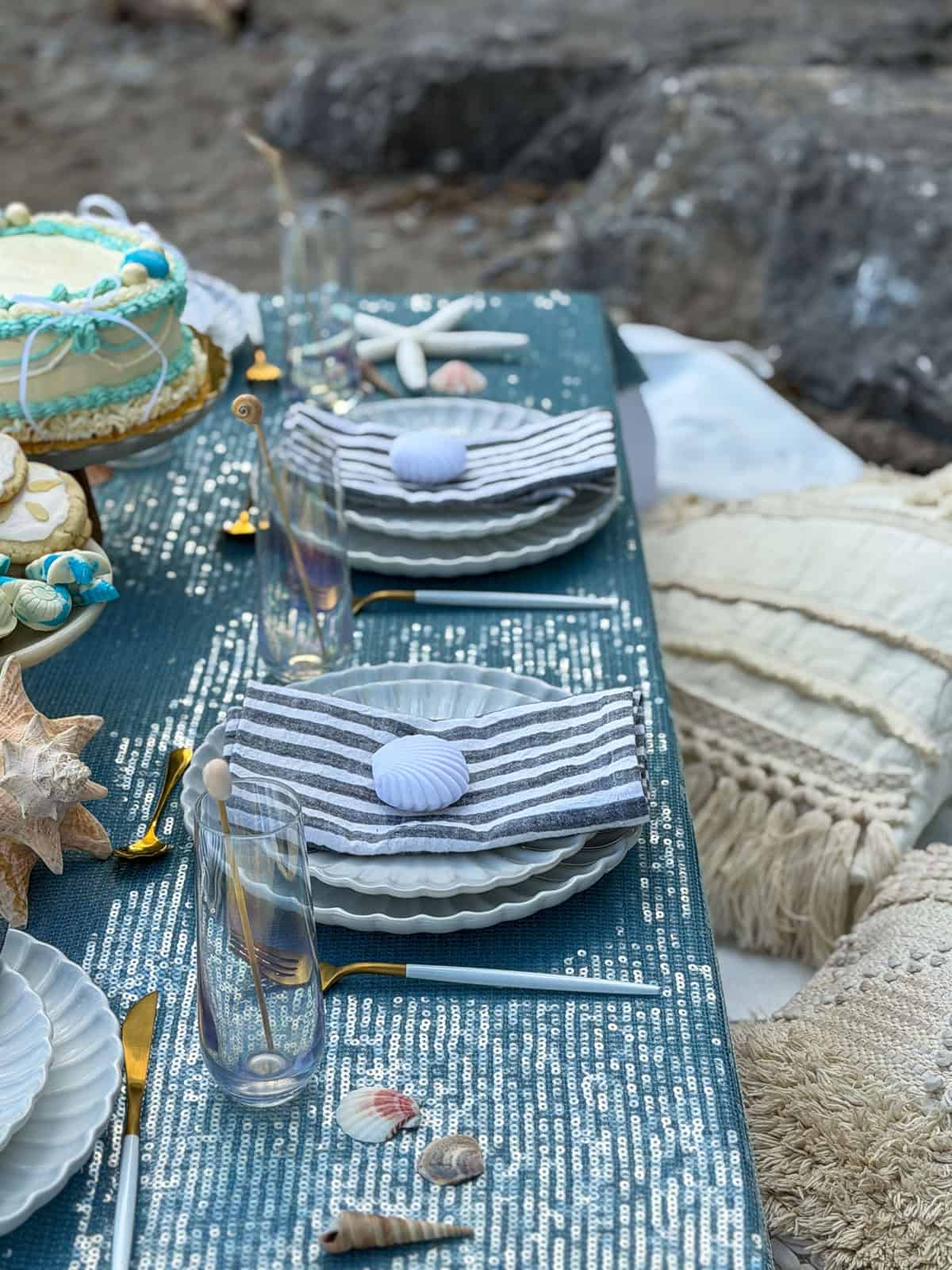 Two beach place settings with striped napkins and seashells.