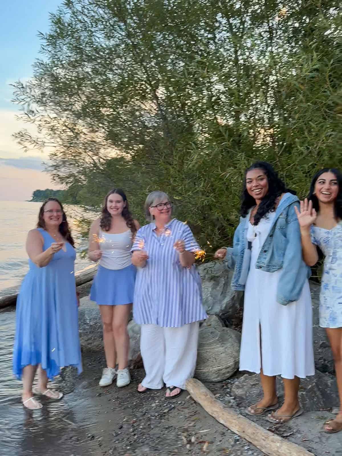Group of women celebrating with sparklers on the beach at sunset.