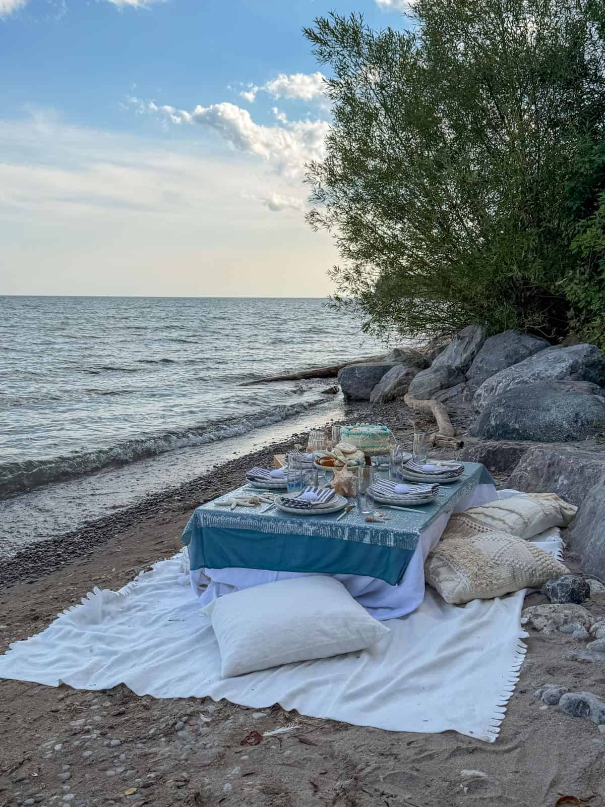 Beach picnic table set near rocks and willow tree on the shoreline.