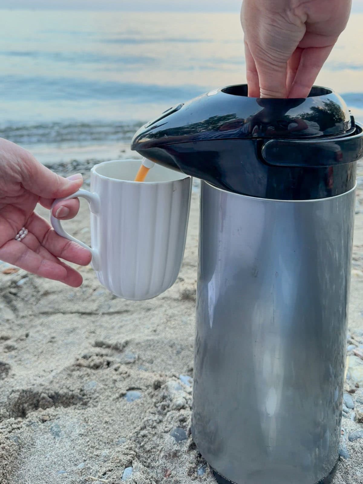 Pouring hot tea from a thermos into a mug at the beach.