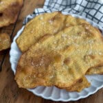 Two golden brown flatbread crackers with cracked pepper and flaky sea salt on a white scalloped plate.