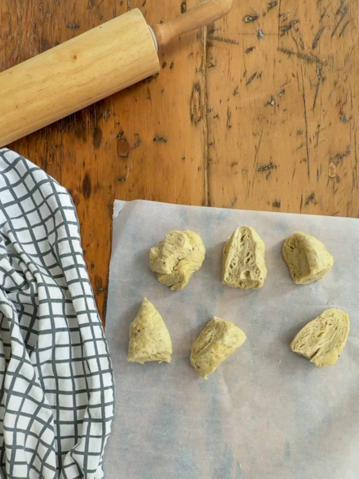 Six pieces of flatbread cracker dough divided and shaped on parchment paper, ready to roll.