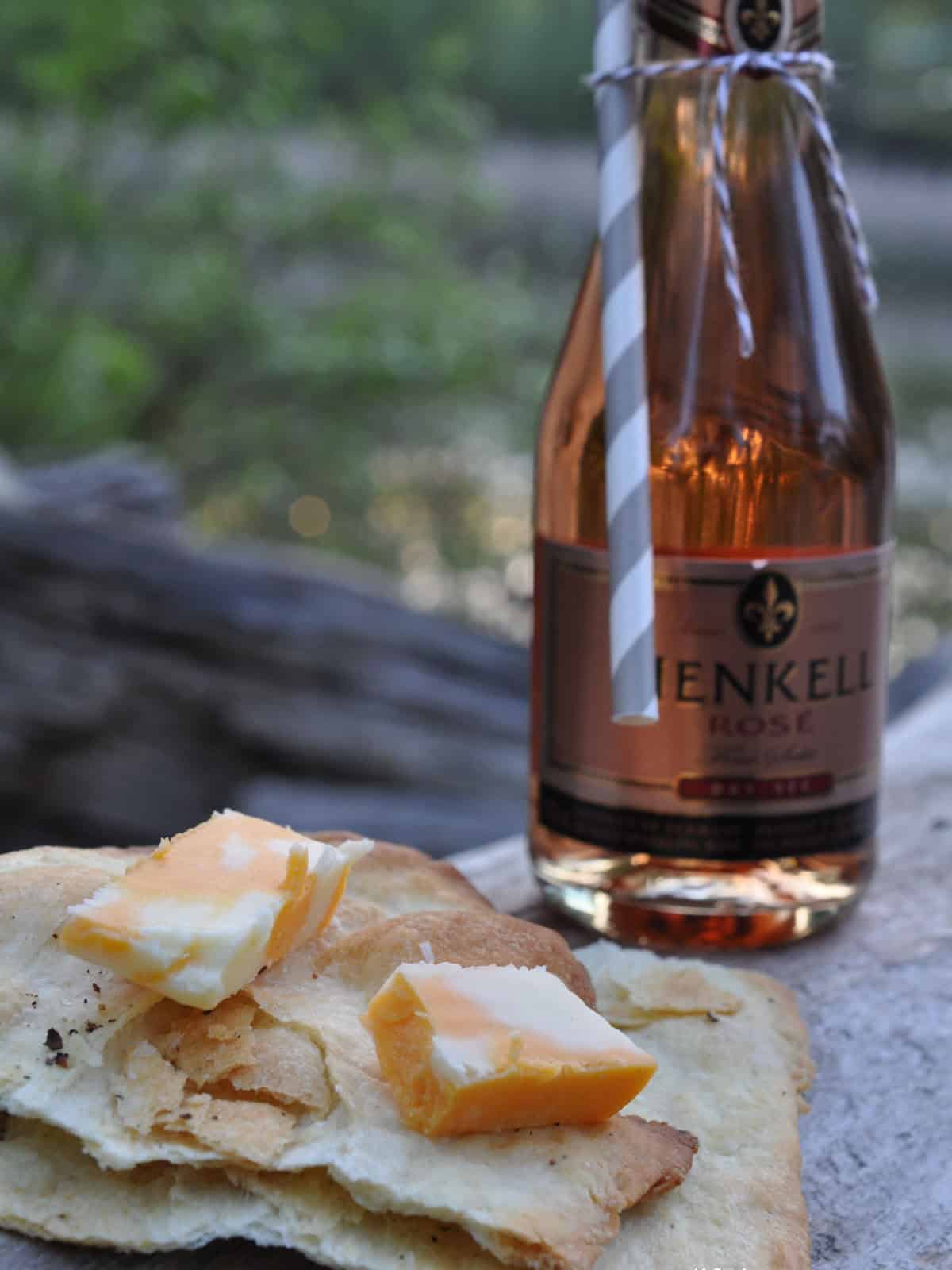 Cubed cheddar and Havarti cheese on a flatbread cracker recipe with a bottle of rosé in the background.