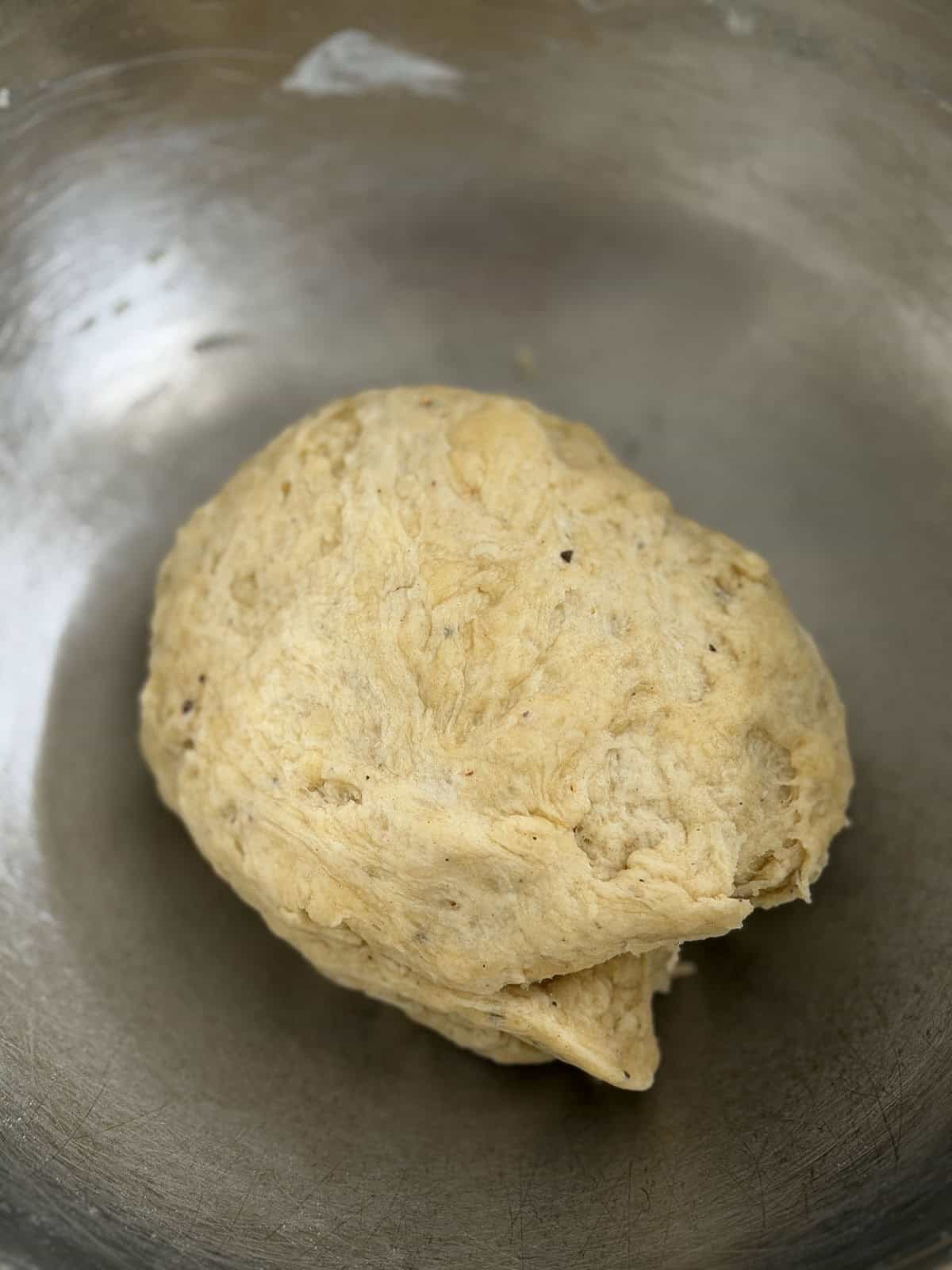 Smooth ball of kneaded flatbread cracker dough in a stainless steel bowl.