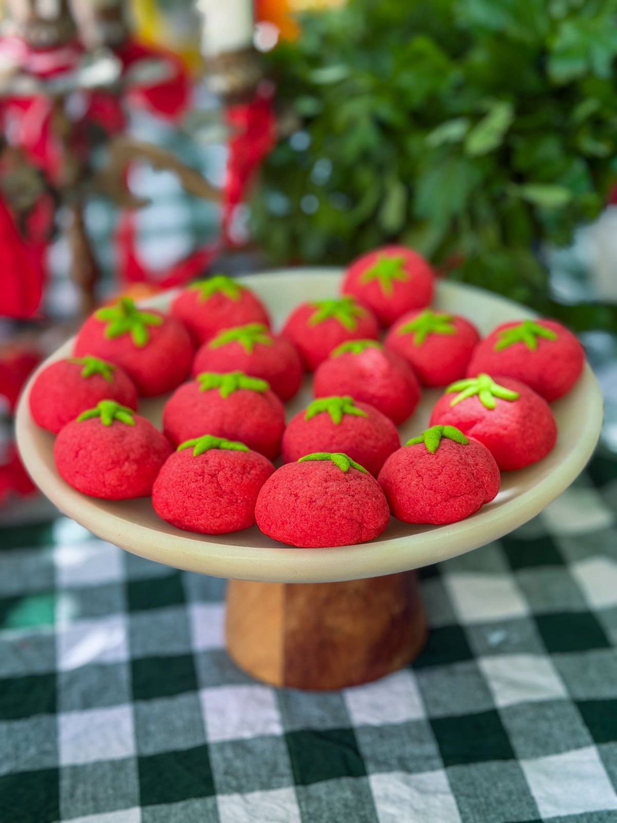 Tomato shaped sugar cookies with green stems on cake stand.