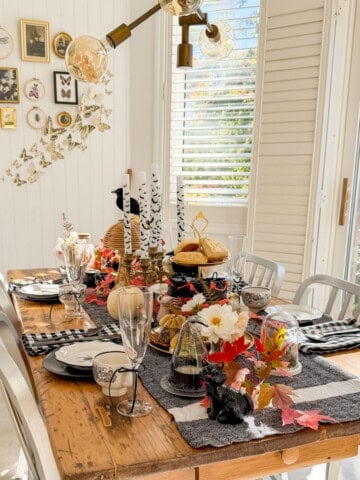 Witch tea party table with a tiered tray of scones and black cakes, bat candles, a black cat figurine and a gallery wall behind.