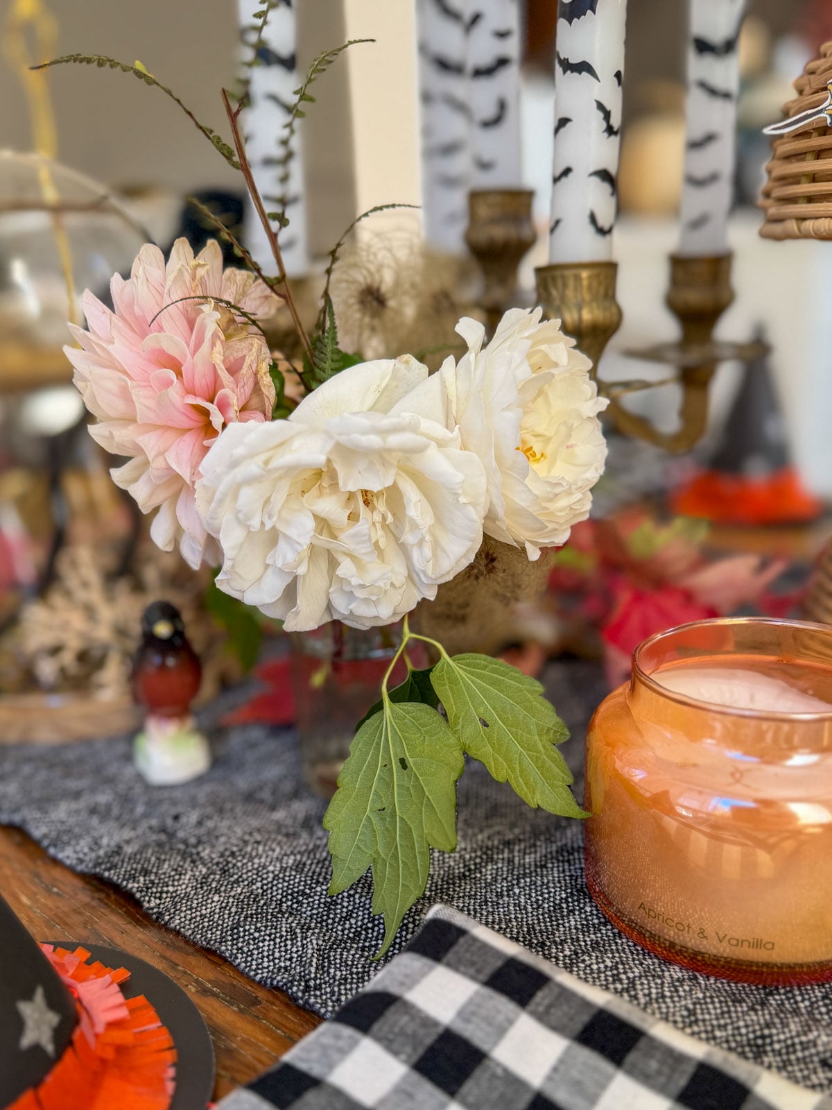 Pink dahlia and white roses in a small glass vase with fern and fall leaves.