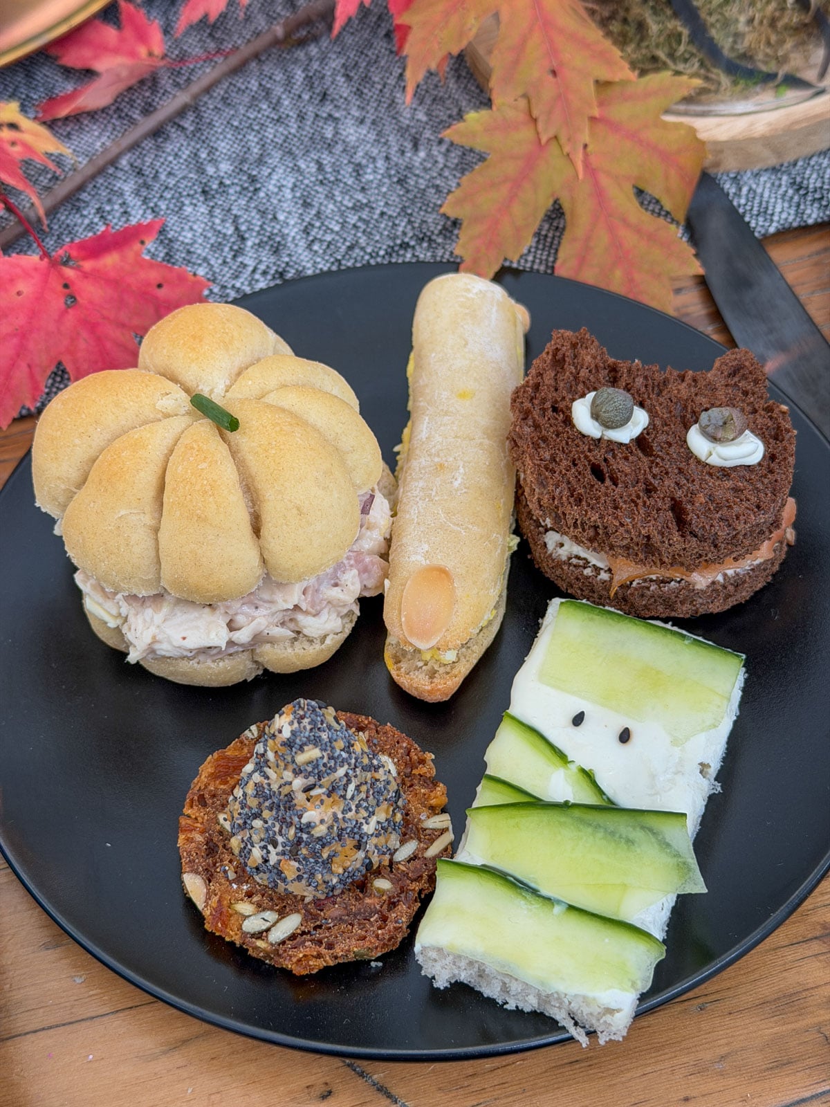One guest’s portion of the witch tea party menu on a black plate, with a pumpkin roll, witch finger, cat sandwich, mummy sandwich and cheese hat cracker.