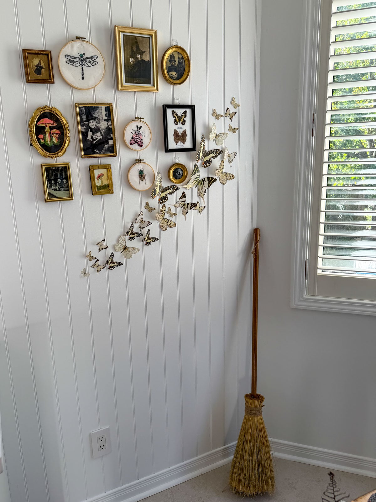 Gallery wall with a straw broom standing in the corner beside it.