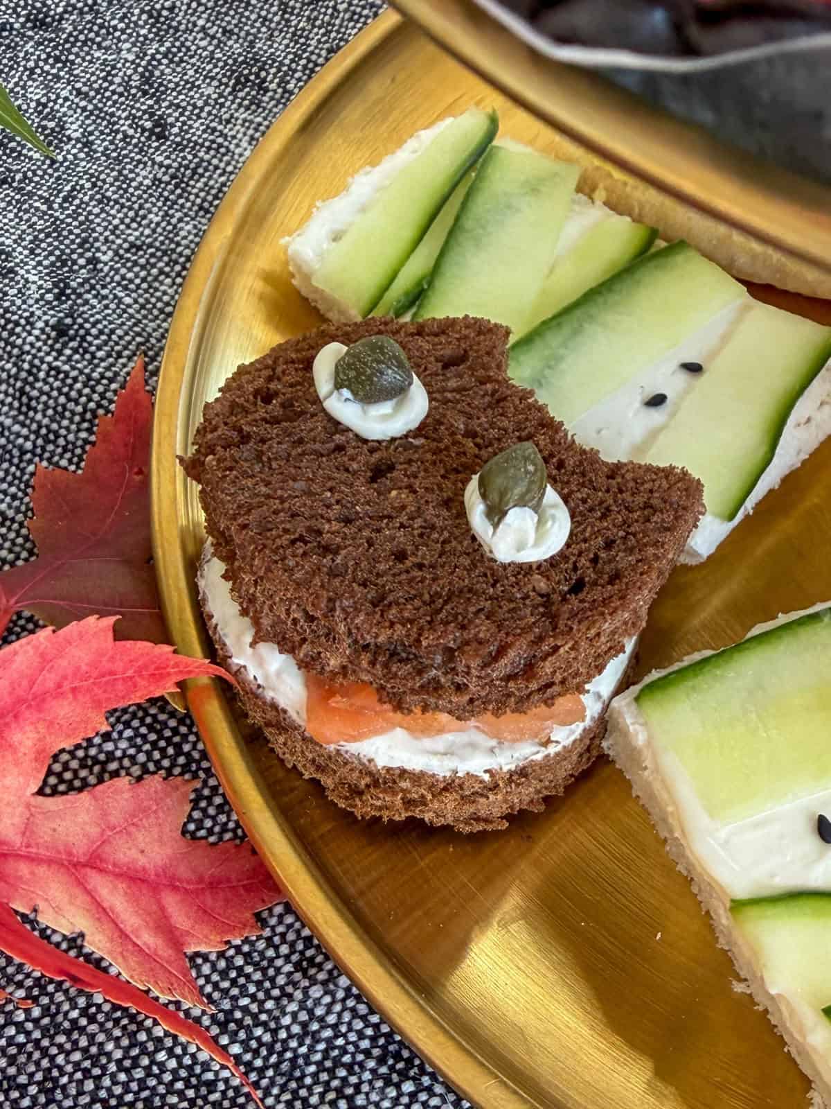 Pumpernickel sandwiches cut into cat shapes with salmon and caper eyes.