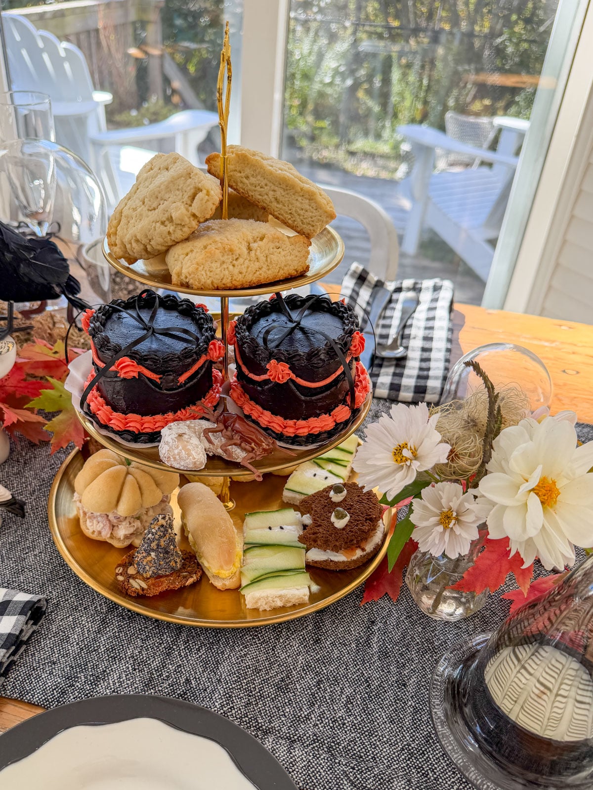 Three tier tray with sandwiches on the bottom, black cakes in the middle and scones on top.