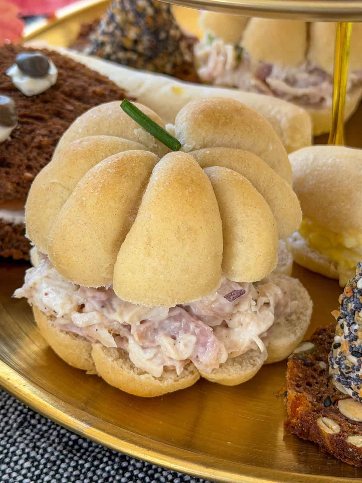 Small pumpkin shaped rolls filled with chicken salad on a tiered tray.