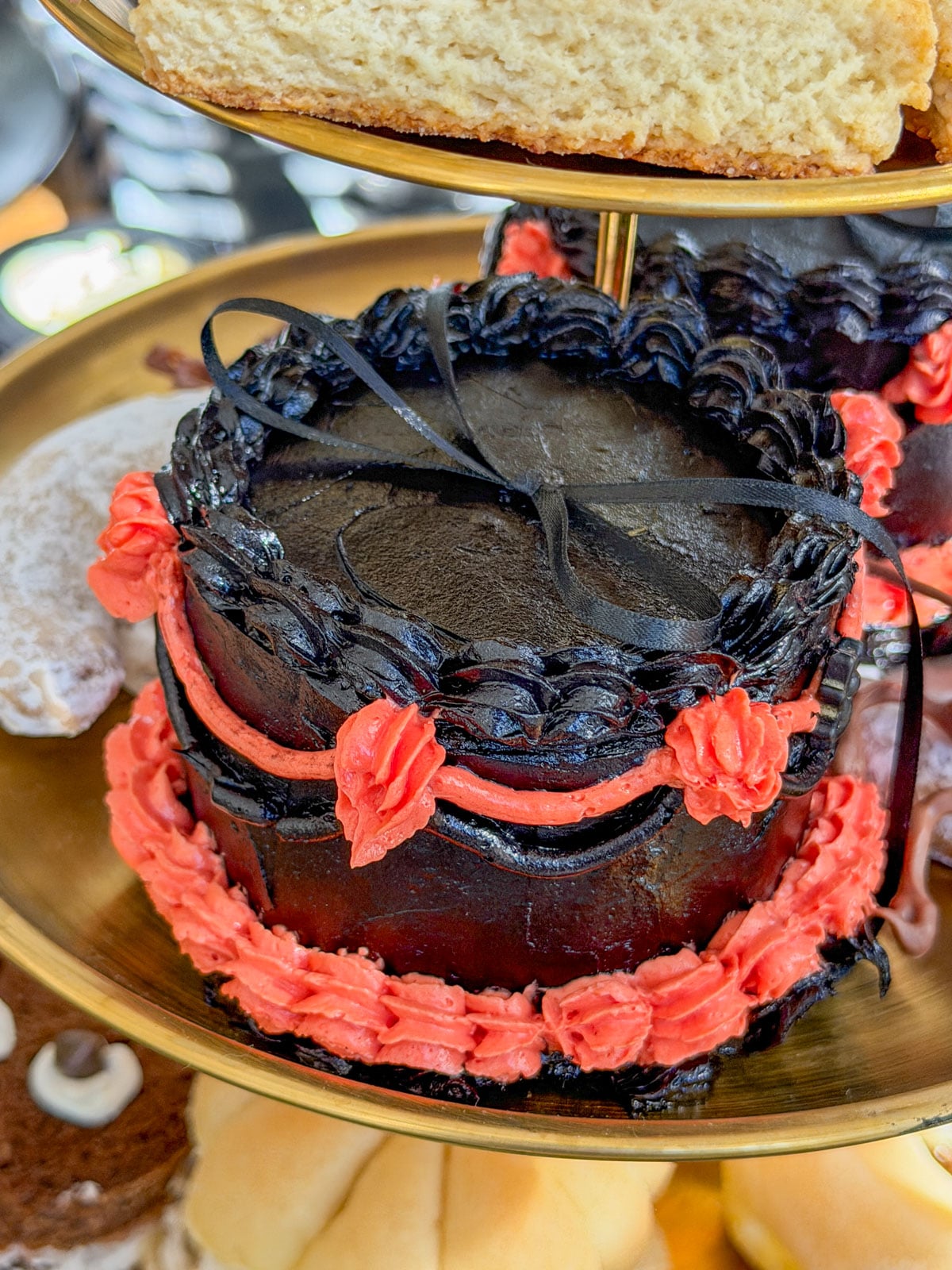 Mini black cake with orange buttercream piping and a black ribbon on a tiered tray.